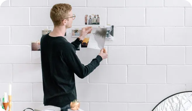 A person in an office sticking various images to a white tiled wall.