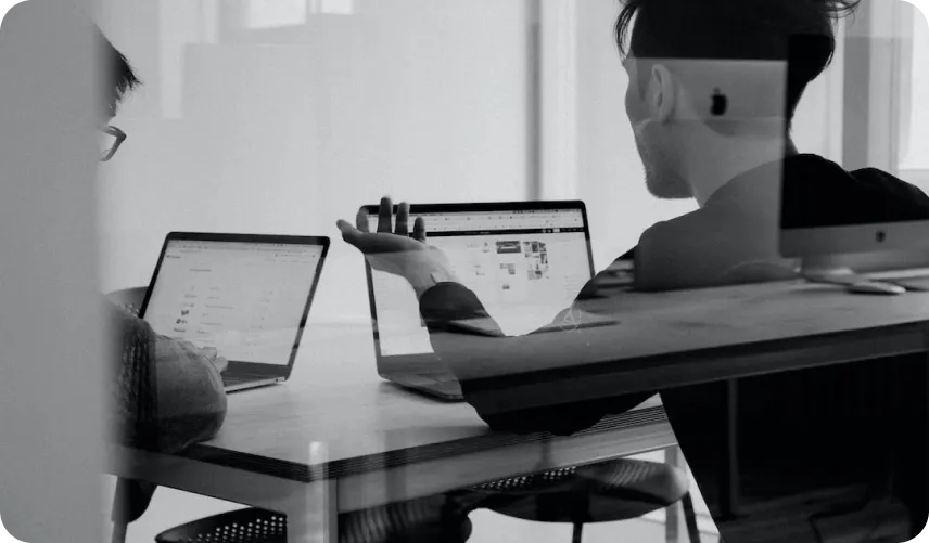 Two people talking and working on two laptops.